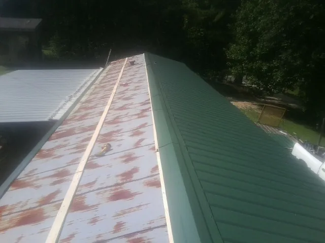 Old rusted panels beside newly installed green metal roofing — Wind Damage Roof Repair by Roofing Brothers in Walnut Cove