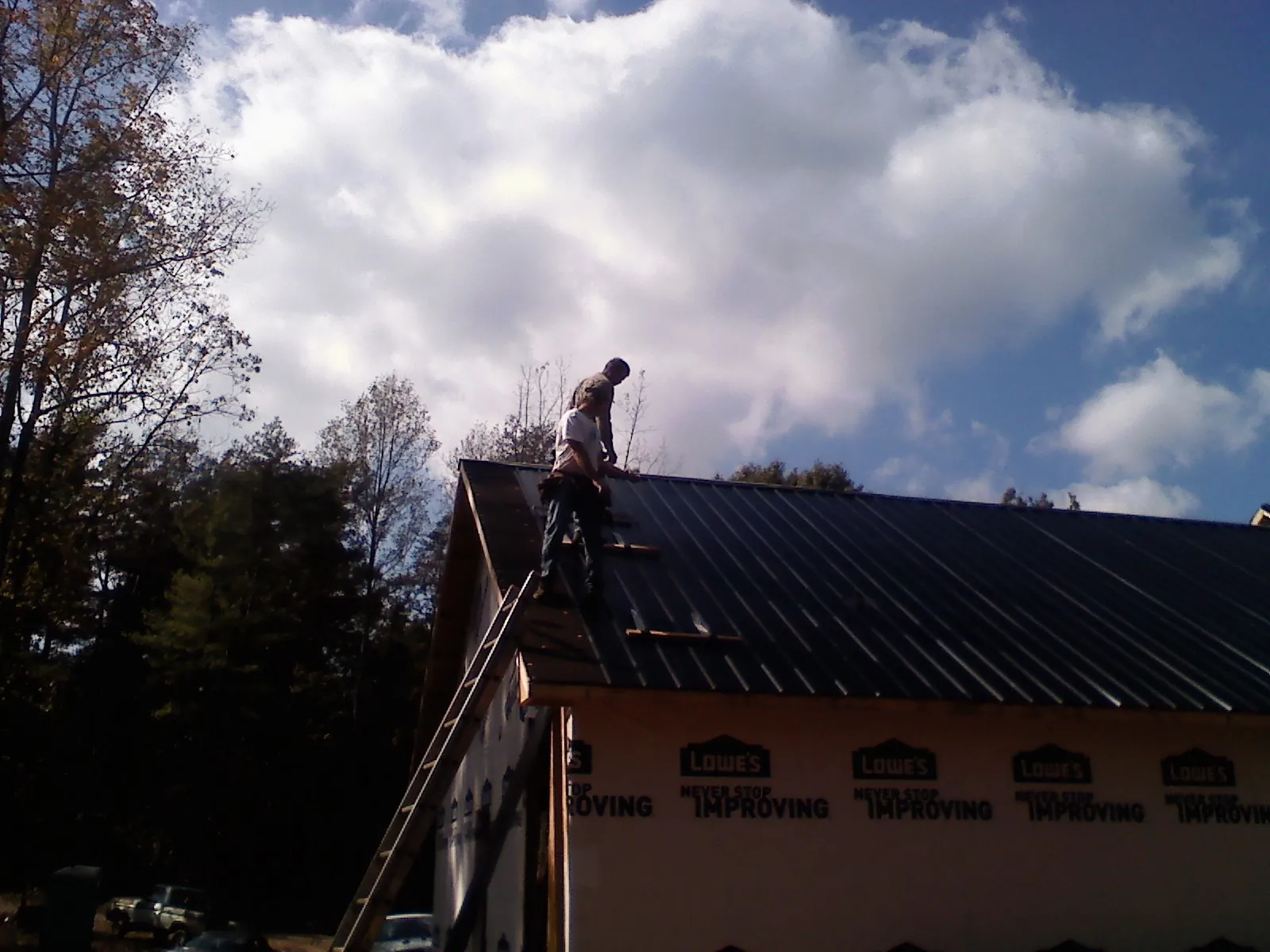 Roofer fastening dark metal panels high against a cloudy sky, from a Roof Inspection job in Walnut Cove