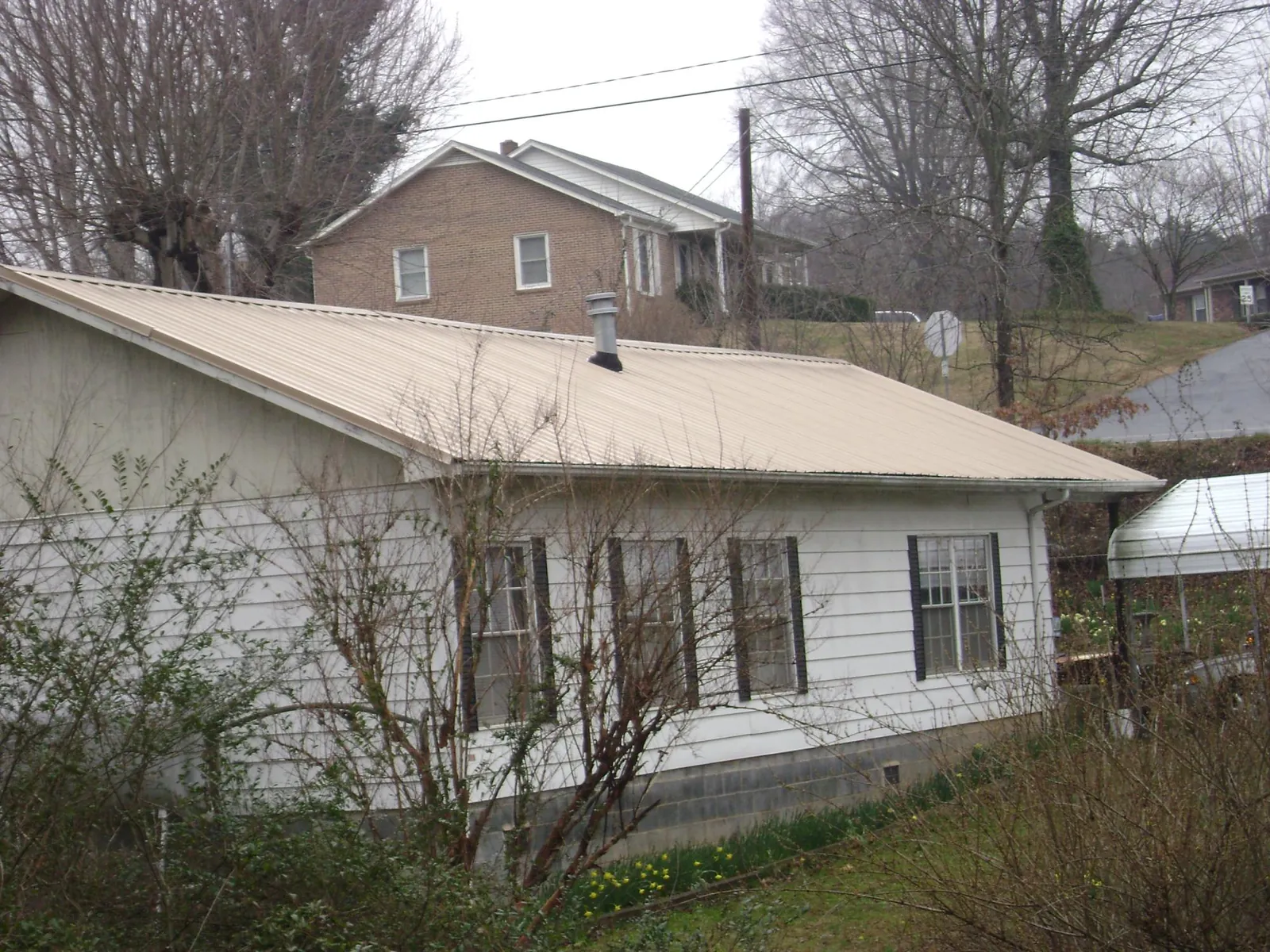 Tan metal roof on a white sided house set into a hillside — Commercial Roofing by Roofing Brothers in Walnut Cove