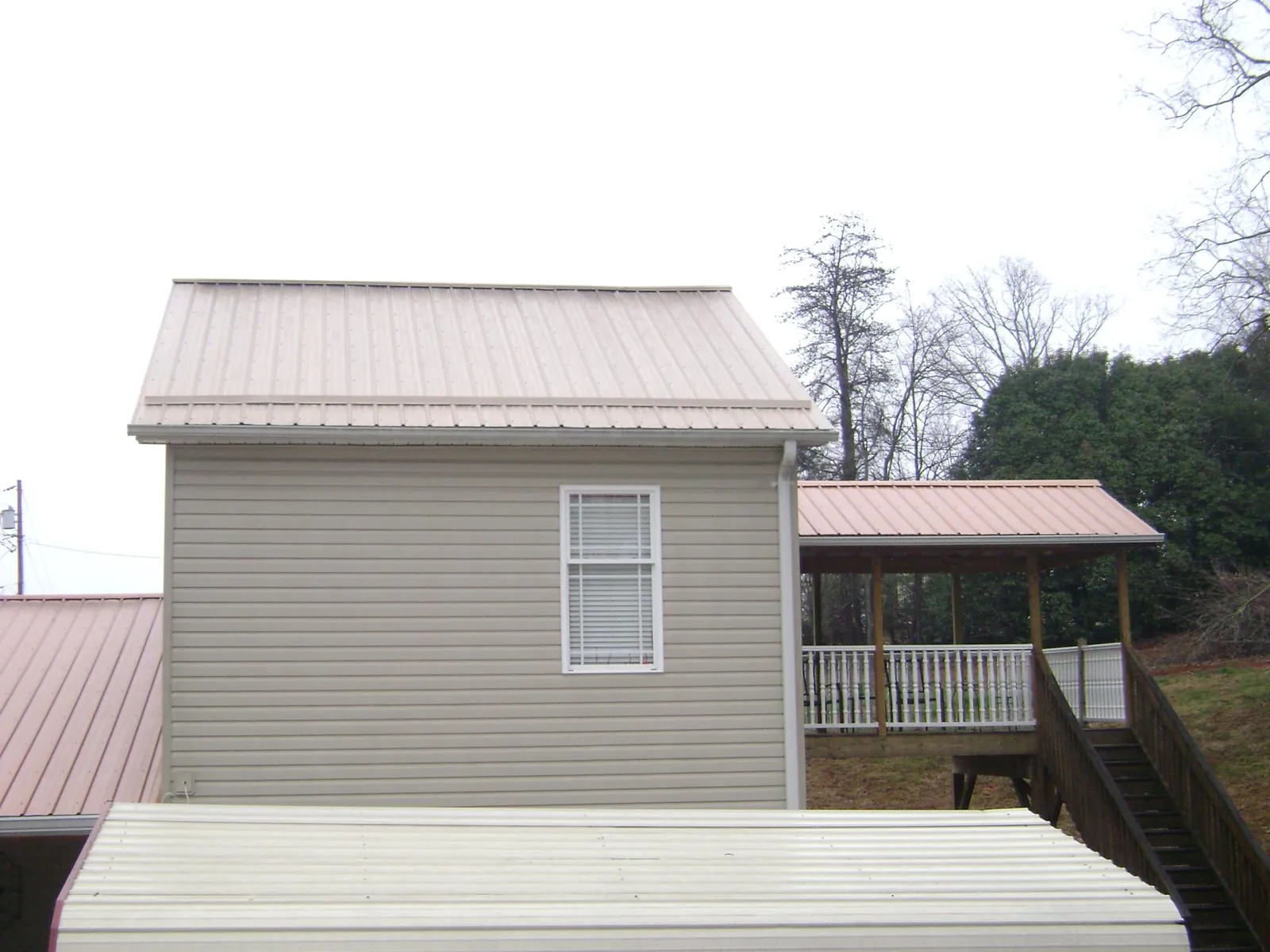 Tan metal roofs on a two story addition and attached porch, from a Roof Replacement job in Walnut Cove