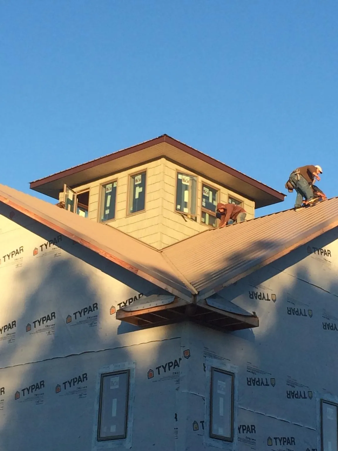 Roofers working around a rooftop cupola on a new metal roof at sunset in Walnut Cove